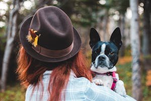 A woman in a hat holding a Boston Terrier outdoors