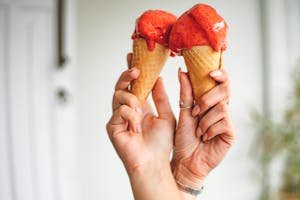 Close-up of two hands holding strawberry ice cream cones.