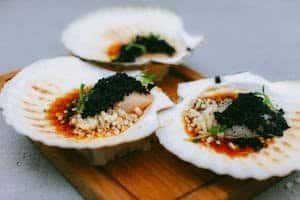 Close-up of gourmet scallops with caviar, served in seashells with sauce.