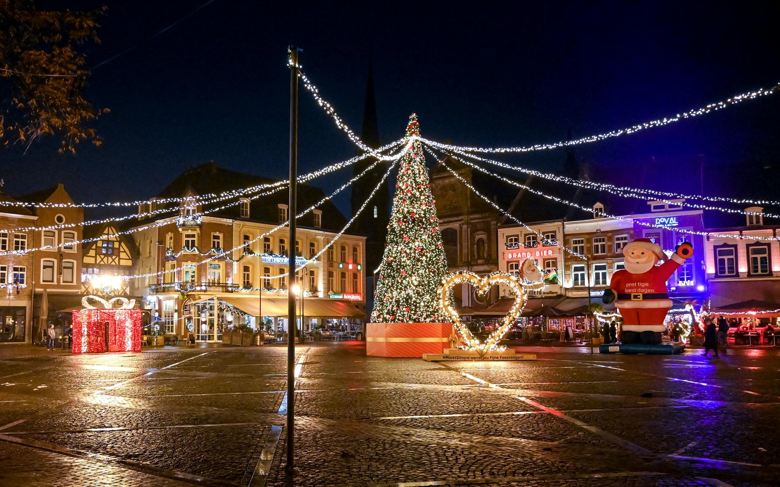 A festive night scene at Christmas market with lights and decorations.