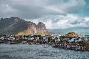 A stunning view of Reine village in Lofoten, Norway, with red cabins, a rainbow, and majestic mountains.
