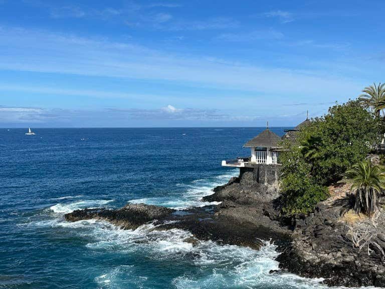 Beautiful coastline with waves crashing on rocks under a clear blue sky in Costa Adeje, Spain.