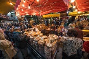 Bustling market scene at London's Borough Market with crowds buying artisan bread under colorful umbrellas.