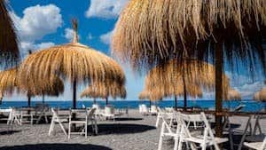 Serene beach scene with thatched umbrellas and chairs under a sunny sky in Adeje, Spain.