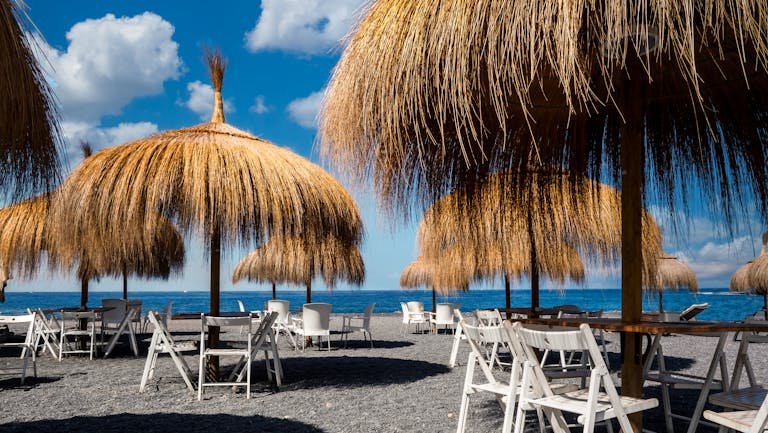 Serene beach scene with thatched umbrellas and chairs under a sunny sky in Adeje, Spain.