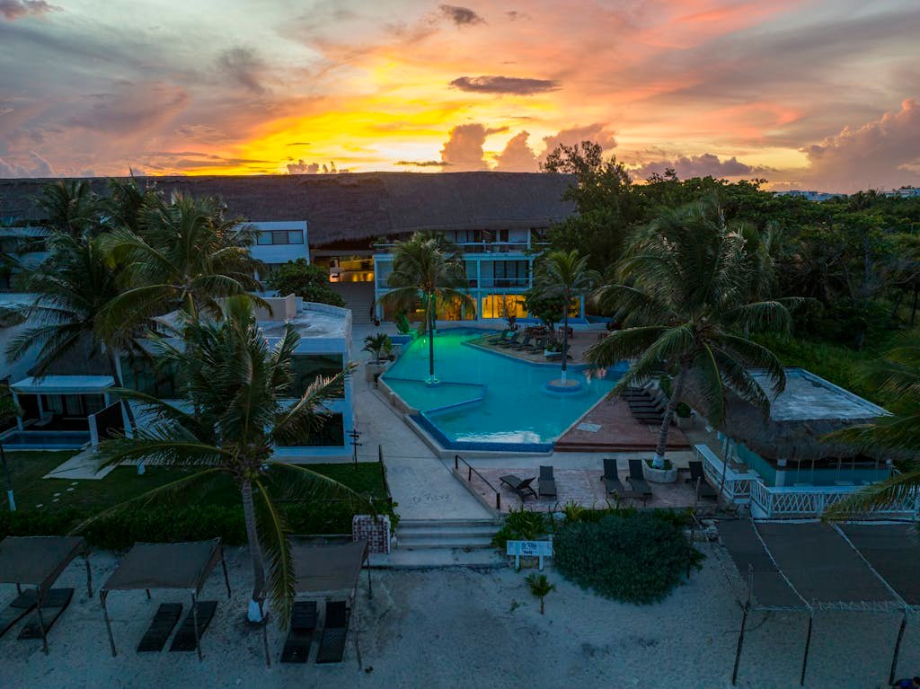 Aerial view of a luxurious tropical resort with a pool at sunset in Playa del Carmen.