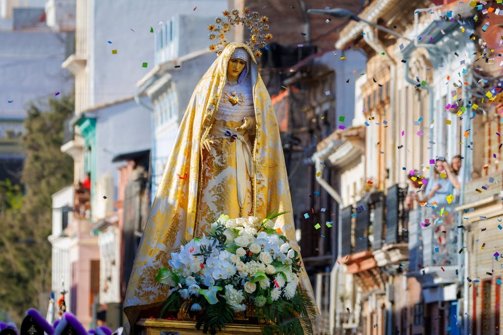 Decorated Virgin Mary statue with flowers amidst confetti on vibrant street parade.