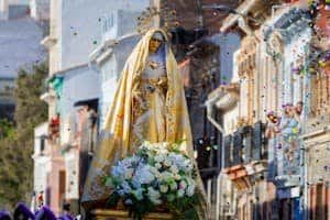 Decorated Virgin Mary statue with flowers amidst confetti on vibrant street parade.