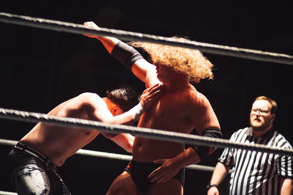 Dramatic wrestling scene with referee coaching competitors in the ring.