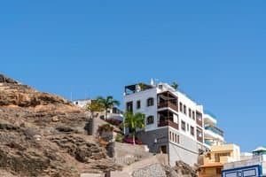 From below of contemporary white residential house built on rocky hill slope against cloudless blue sky on sunny day