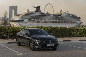 Black luxury car parked with a majestic cruise ship background in Dubai's iconic skyline.