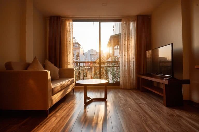 Cozy sunlit living room in Hanoi with minimalist decor and wooden flooring featuring sofa and large window.